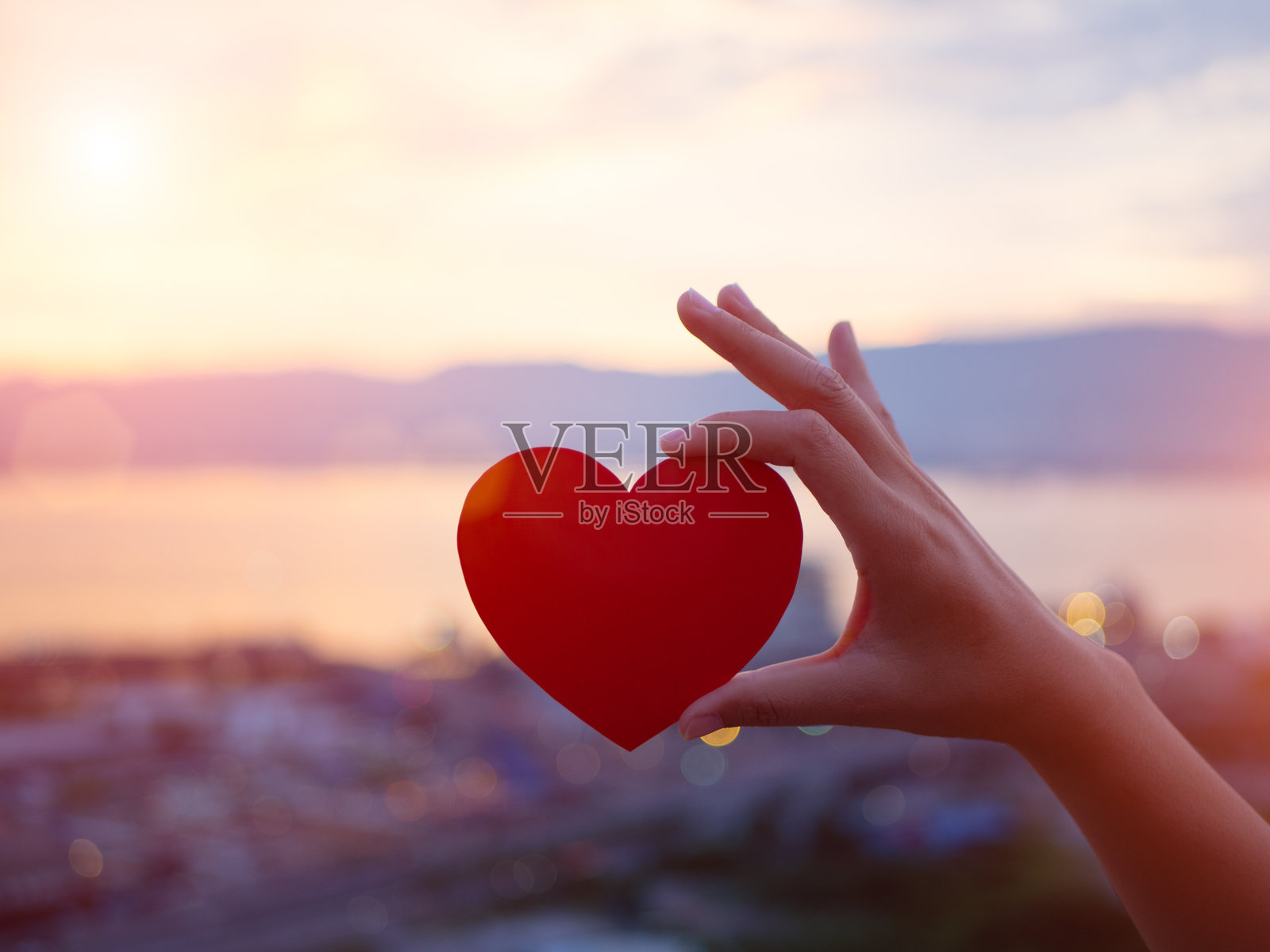 手握红色心形物体对着天空照片摄影图片