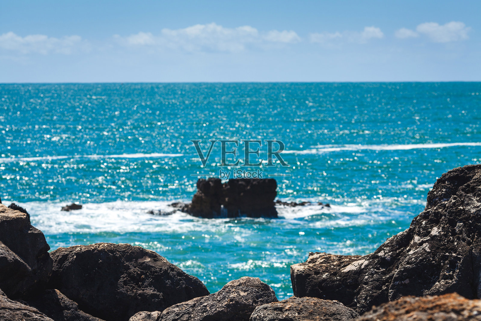 宁静的海洋场景，波光粼粼的蓝色海水延伸至地平线，前景有岩石形成，孤独的岩石从波浪中浮现，营造出宁静的氛围。照片摄影图片