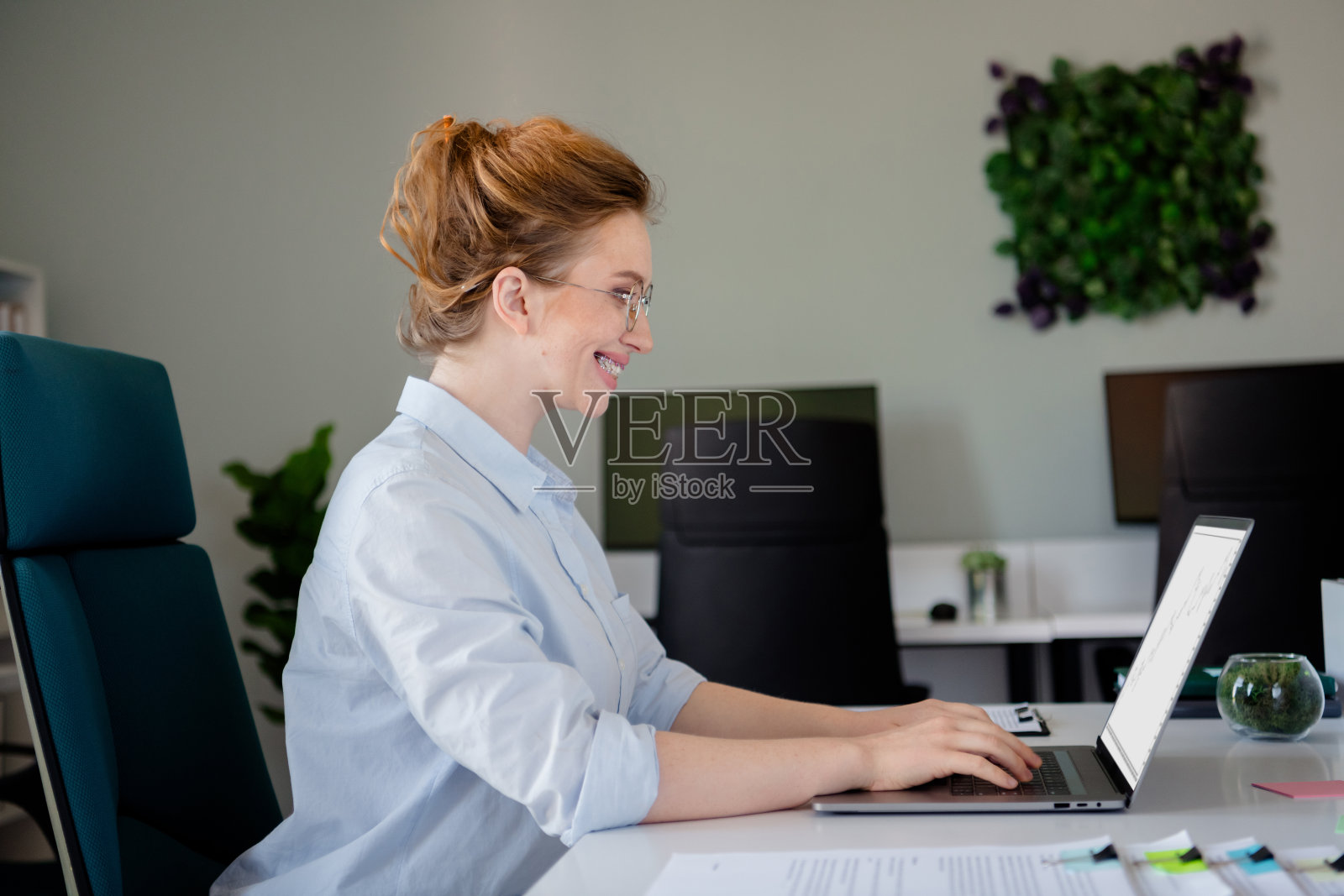 穿着正式商务服装的年轻女士在舒适的初创公司办公室内使用笔记本电脑打字。照片摄影图片