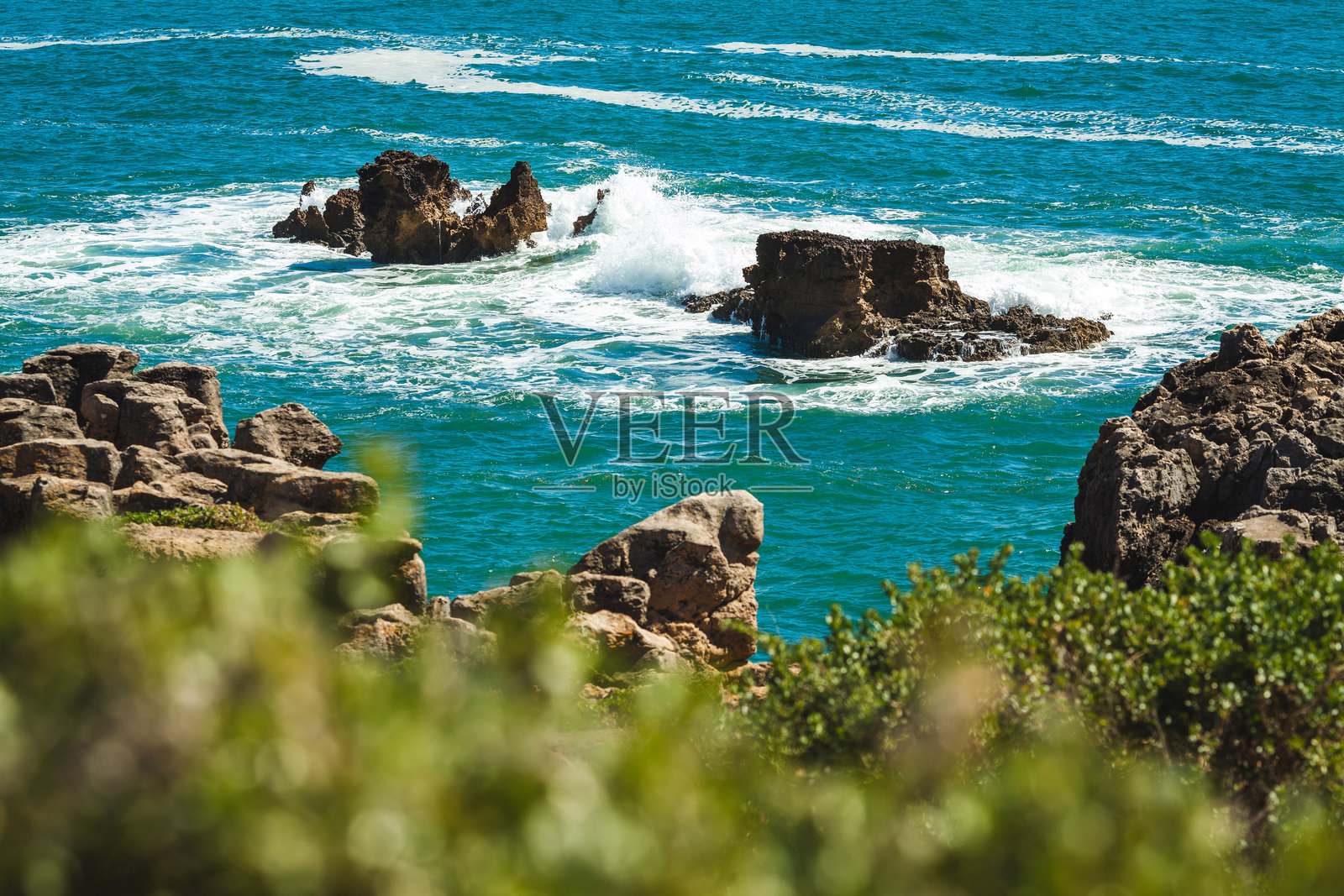 宁静的海洋场景，波光粼粼的蓝色海水延伸至地平线，前景有岩石形成，孤独的岩石从波浪中浮现，营造出宁静的氛围。照片摄影图片