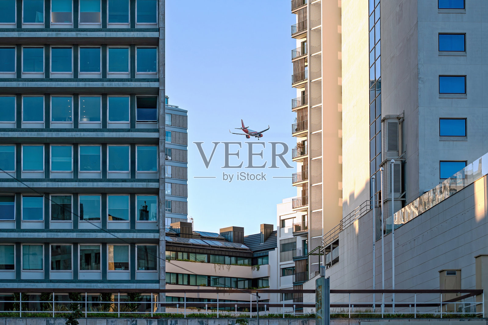 在晴朗的日子里,飞机在现代建筑之间低飞,穿越城市景观。照片摄影图片