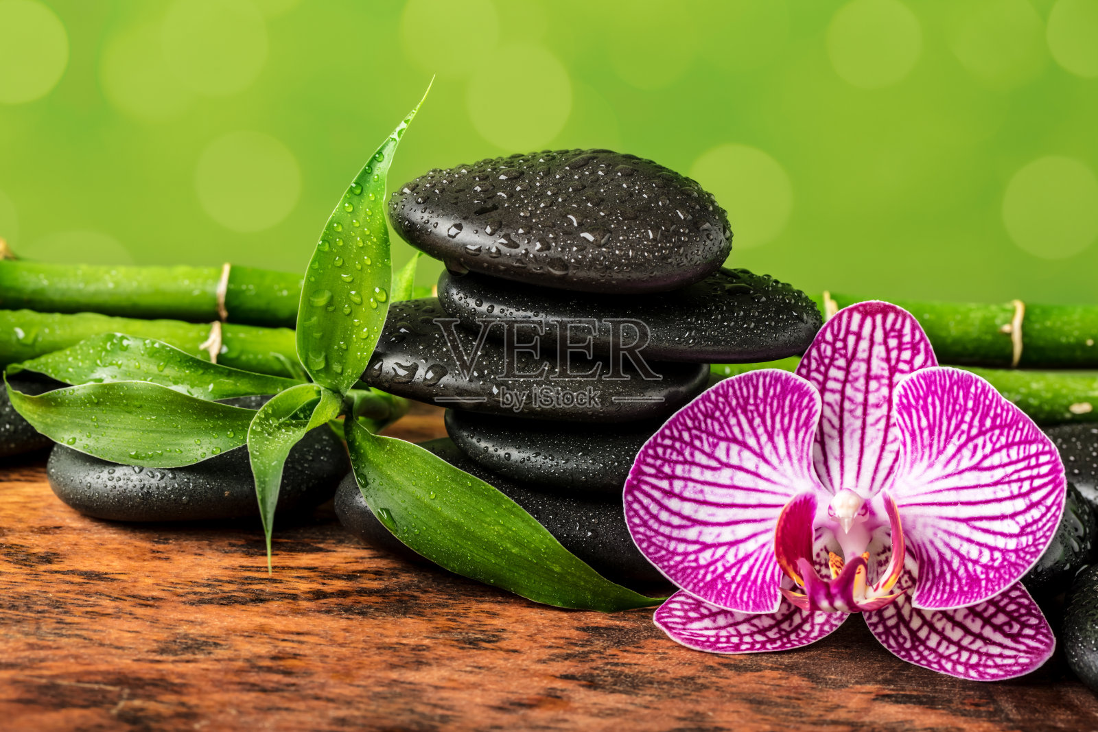 水疗概念 - 黑色按摩石、兰花和竹子在模糊的灯光背景上照片摄影图片