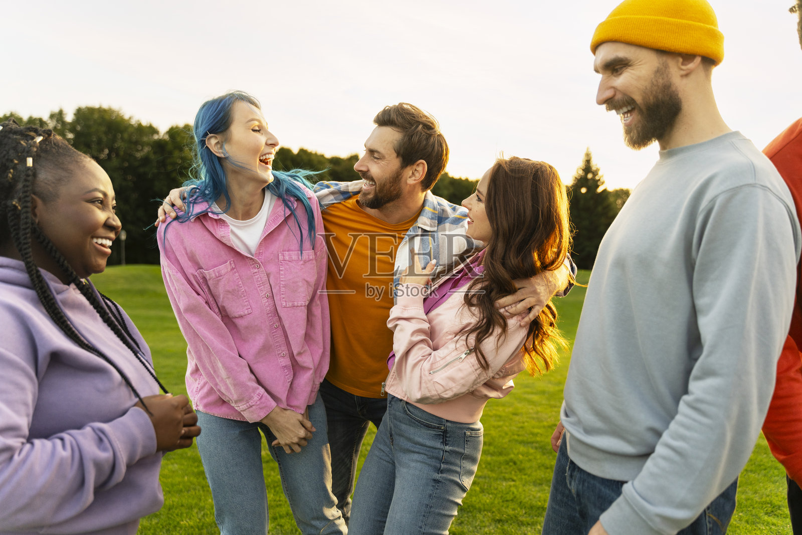 一群多元化的朋友在日落时分的公园里欢笑在一起照片摄影图片