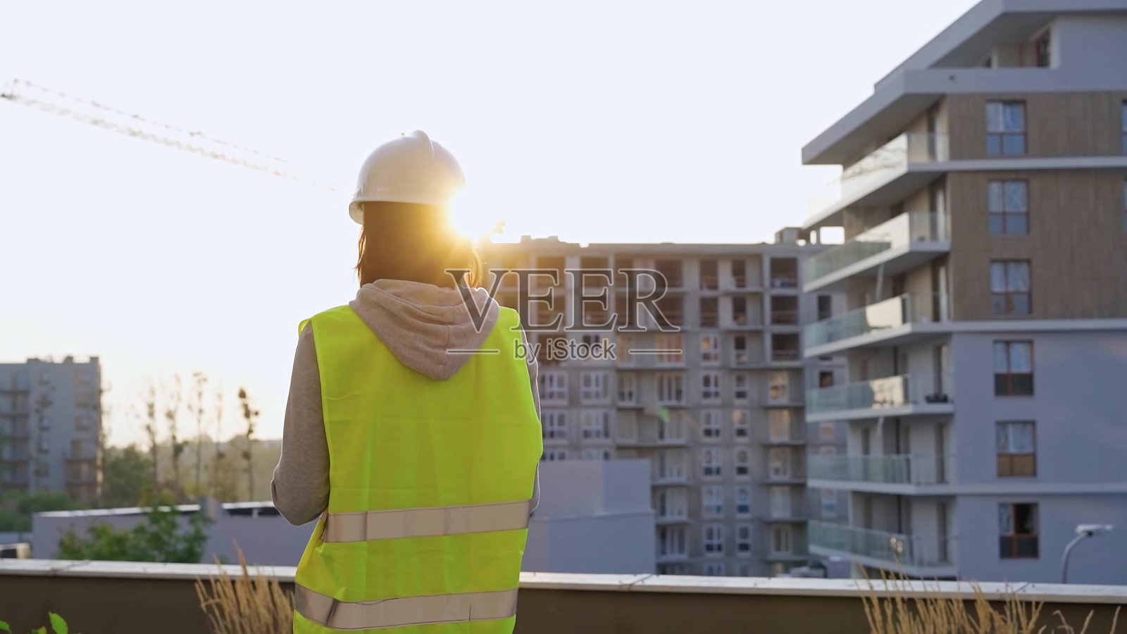 女性工程师在日落时分检查建筑工地，边做笔记边在夹板上写字。照片摄影图片