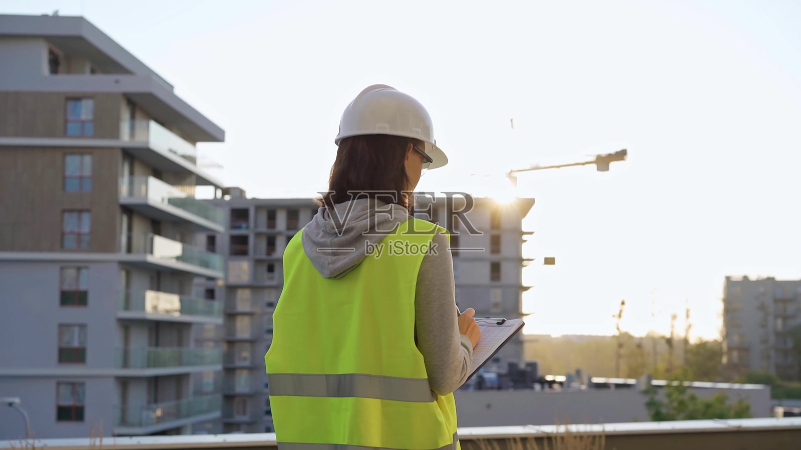 女性建筑工程师在日出时分的清晨检查工地，边记录边在夹板上写字。照片摄影图片