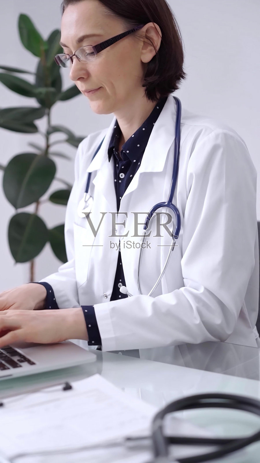 女医生在诊所的玻璃桌上使用笔记本电脑。医生正在输入医疗信息或在线提供建议。医学与药学。照片摄影图片