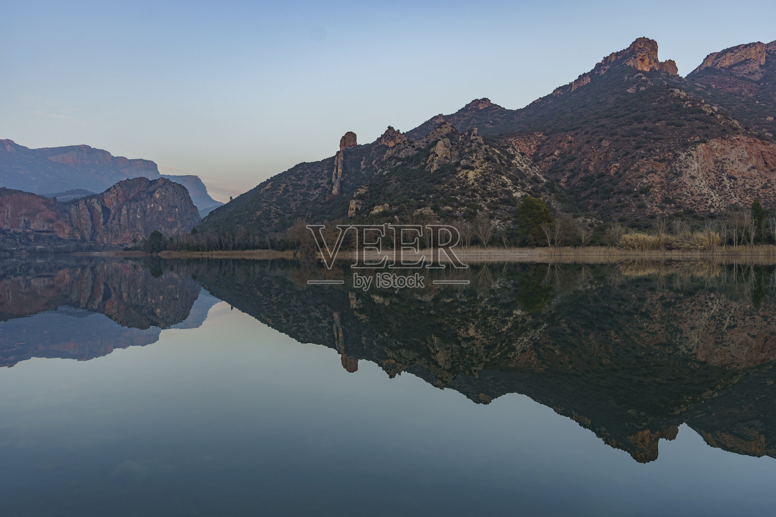 一幅岩石山脉被植被覆盖的景象，倒映在平静湖面的水面上。照片摄影图片