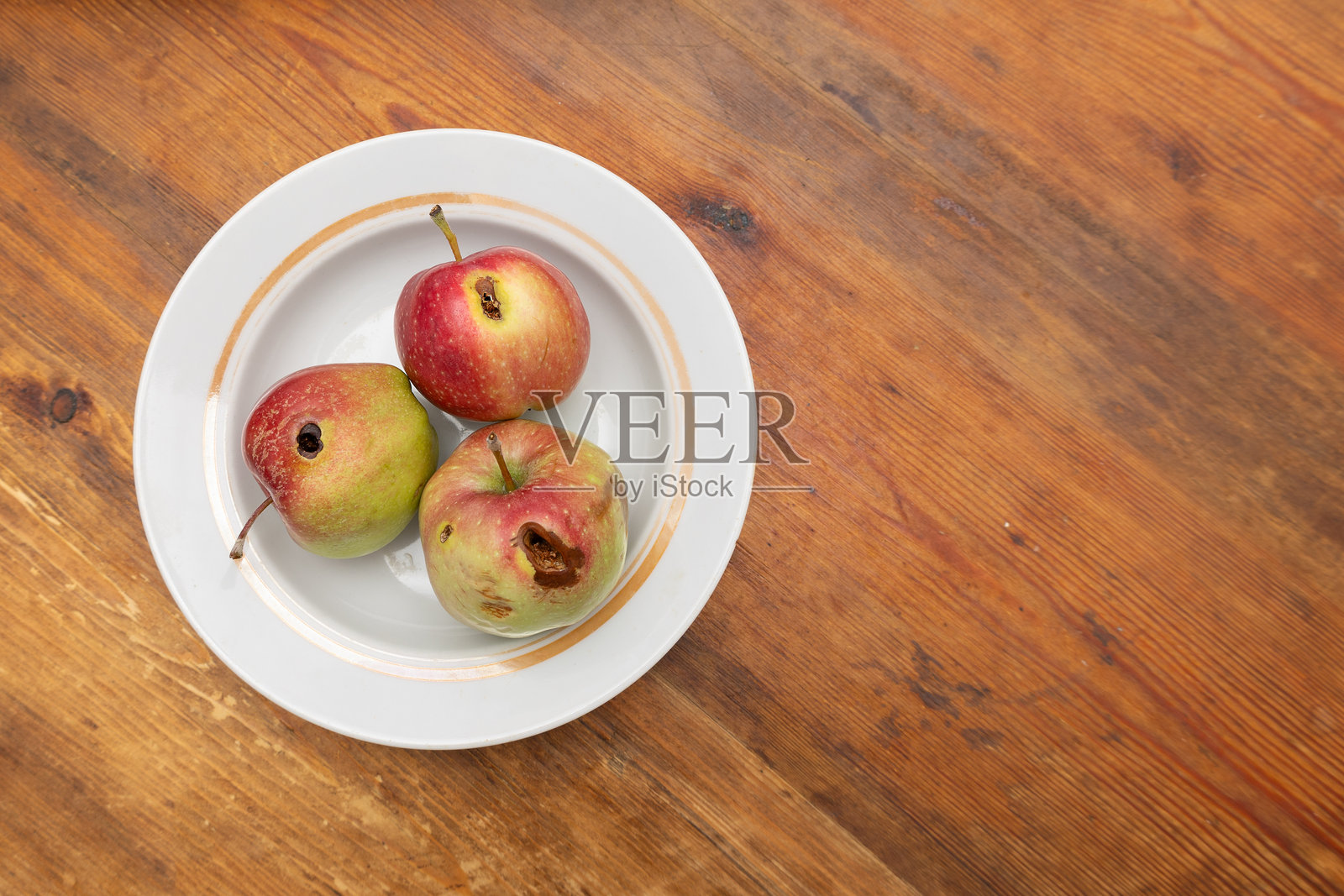 盘子里的腐烂苹果特写，放在木桌上，留有空白空间。照片摄影图片