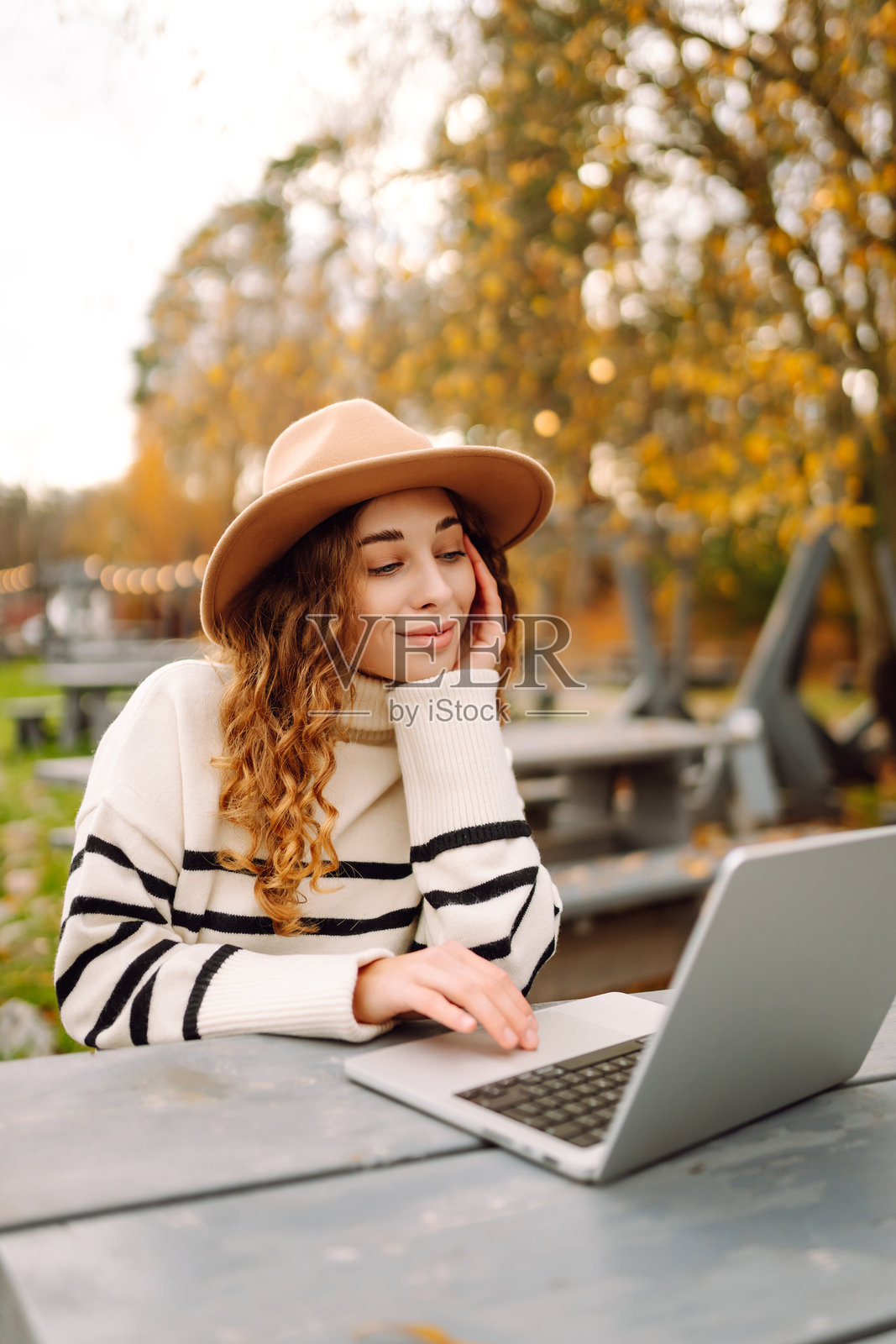 年轻女性在秋天的宁静水道旁的乡村桌子上使用笔记本电脑。照片摄影图片
