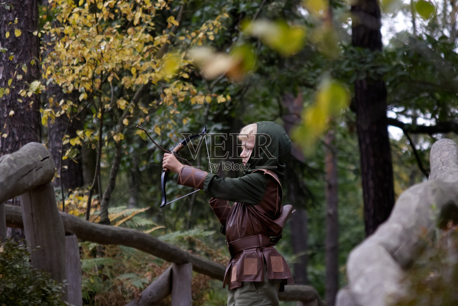 一个穿着中世纪服装的男孩在森林背景下拉着弓弦照片摄影图片