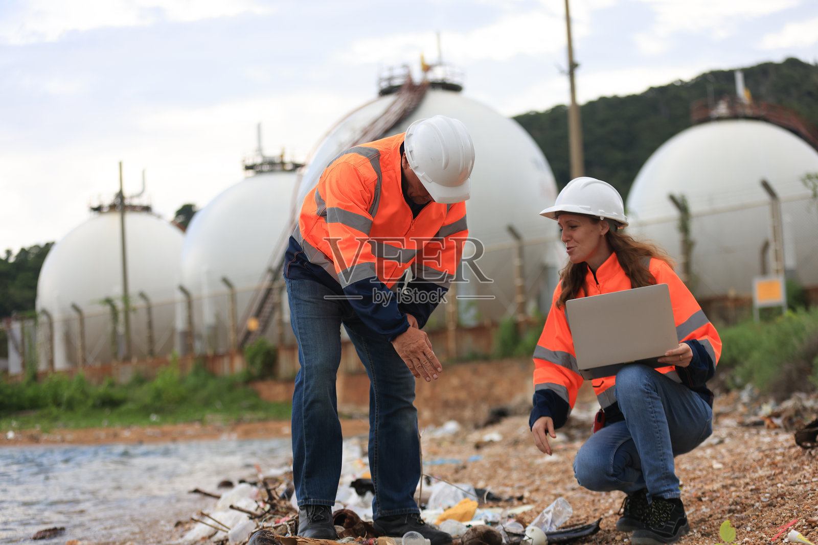 穿着安全工作服的男性和女性高级工程师正在讨论石油和天然气生产性能以及废水研究，使用一台笔记本电脑。照片摄影图片