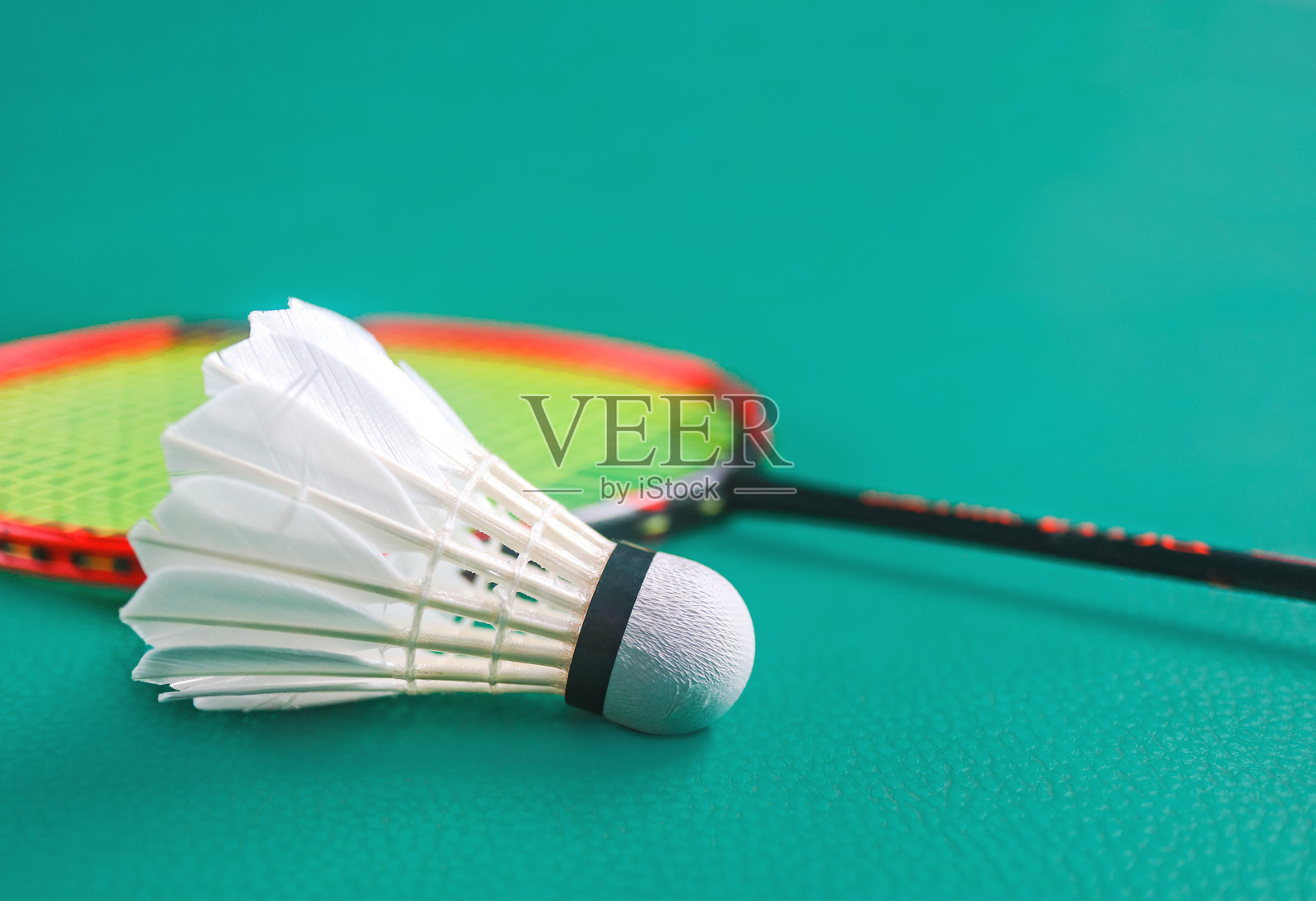 室内羽毛球场绿色地板上的白色羽毛球和羽毛球拍。羽毛球比赛及其爱好者的概念。照片摄影图片