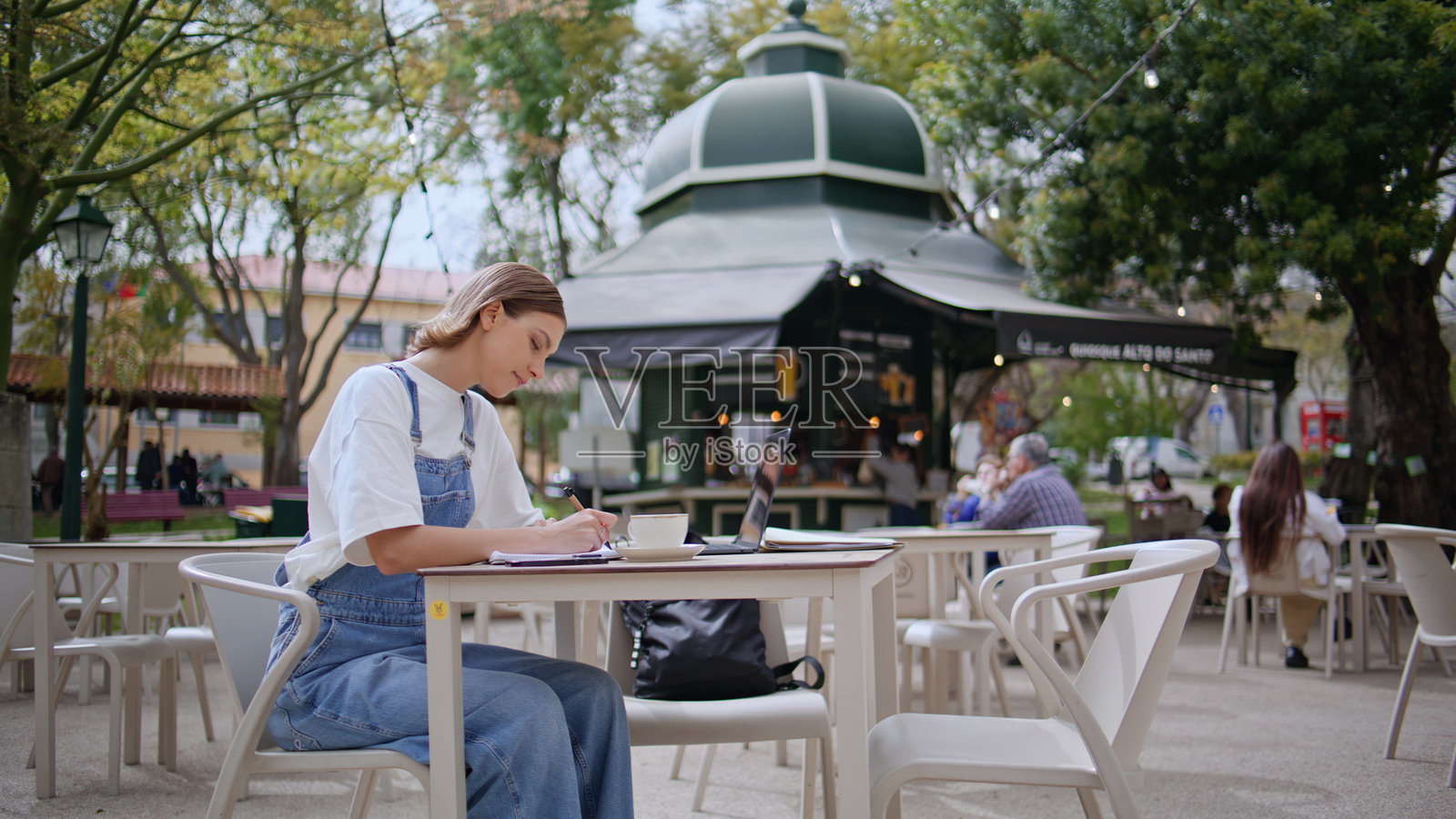 无忧无虑的女性在户外咖啡馆写作。放松的女学生在笔记本电脑上工作。照片摄影图片