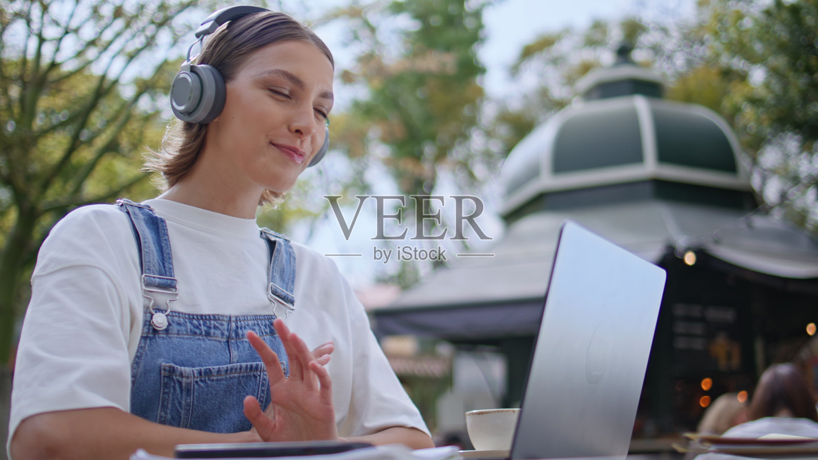 户外近距离特写的女孩戴着耳机，正在通过笔记本电脑摄像头参加虚拟会议。照片摄影图片