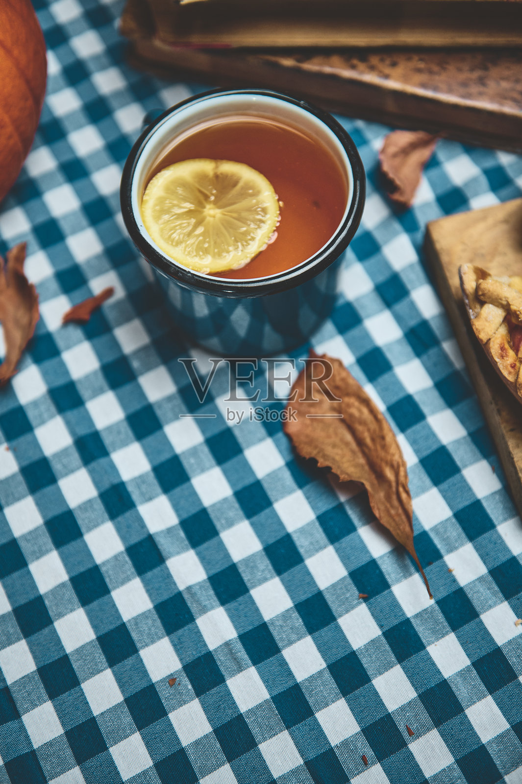 温馨的秋日时光，桌布上放着一杯柠檬热茶，四周环绕着落叶。照片摄影图片