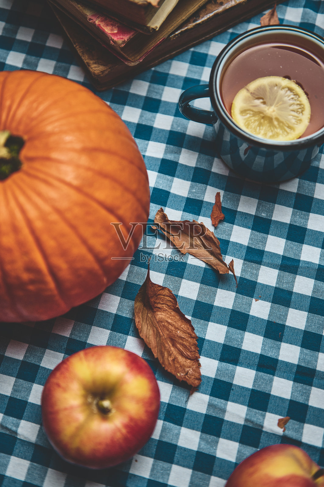 秋季舒适的环境，桌布上摆放着南瓜、苹果和热饮，周围飘落着树叶。照片摄影图片