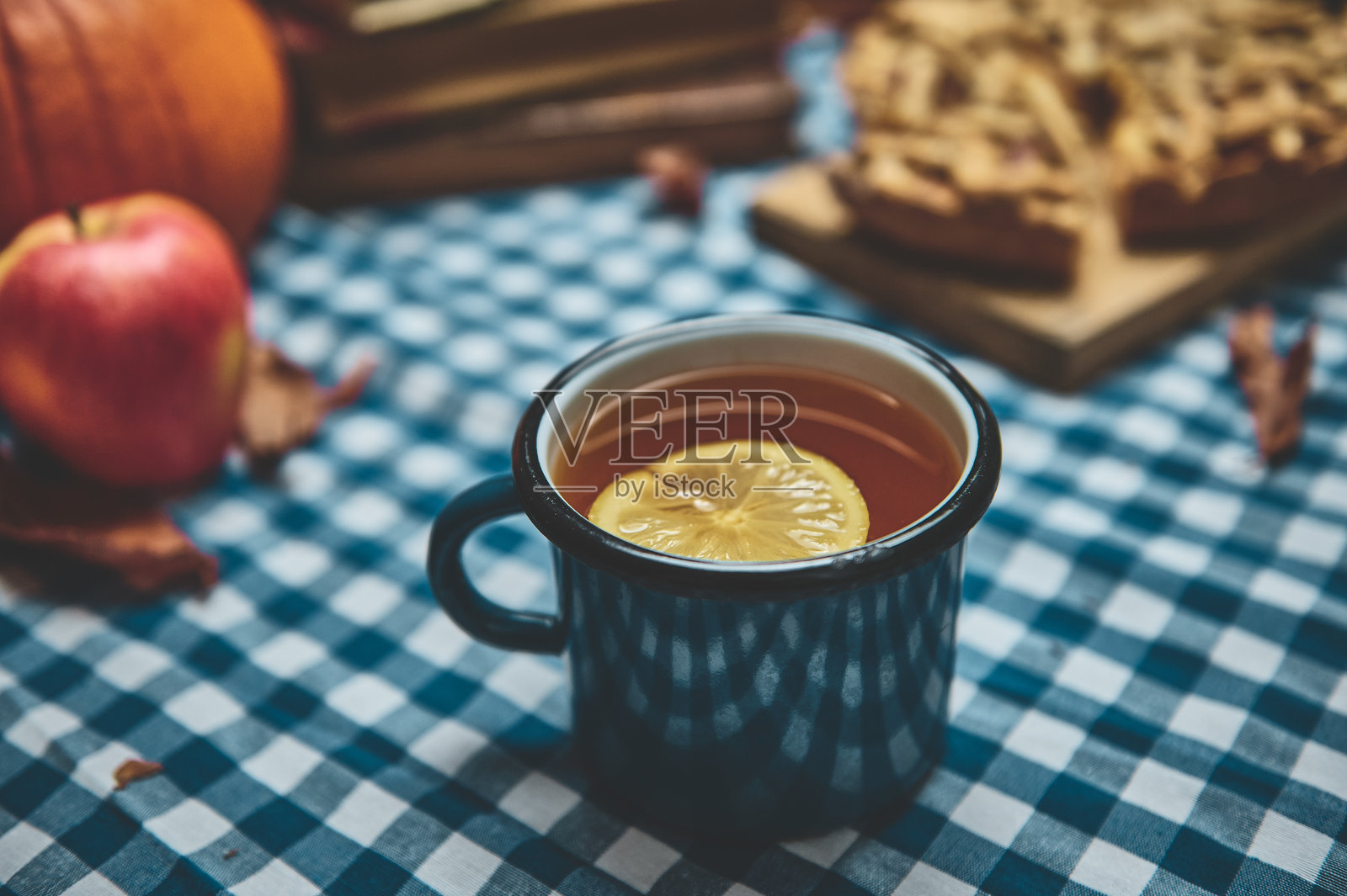 温馨的秋季场景，茶杯旁边围绕着苹果、南瓜和派，放在格子桌布上。照片摄影图片