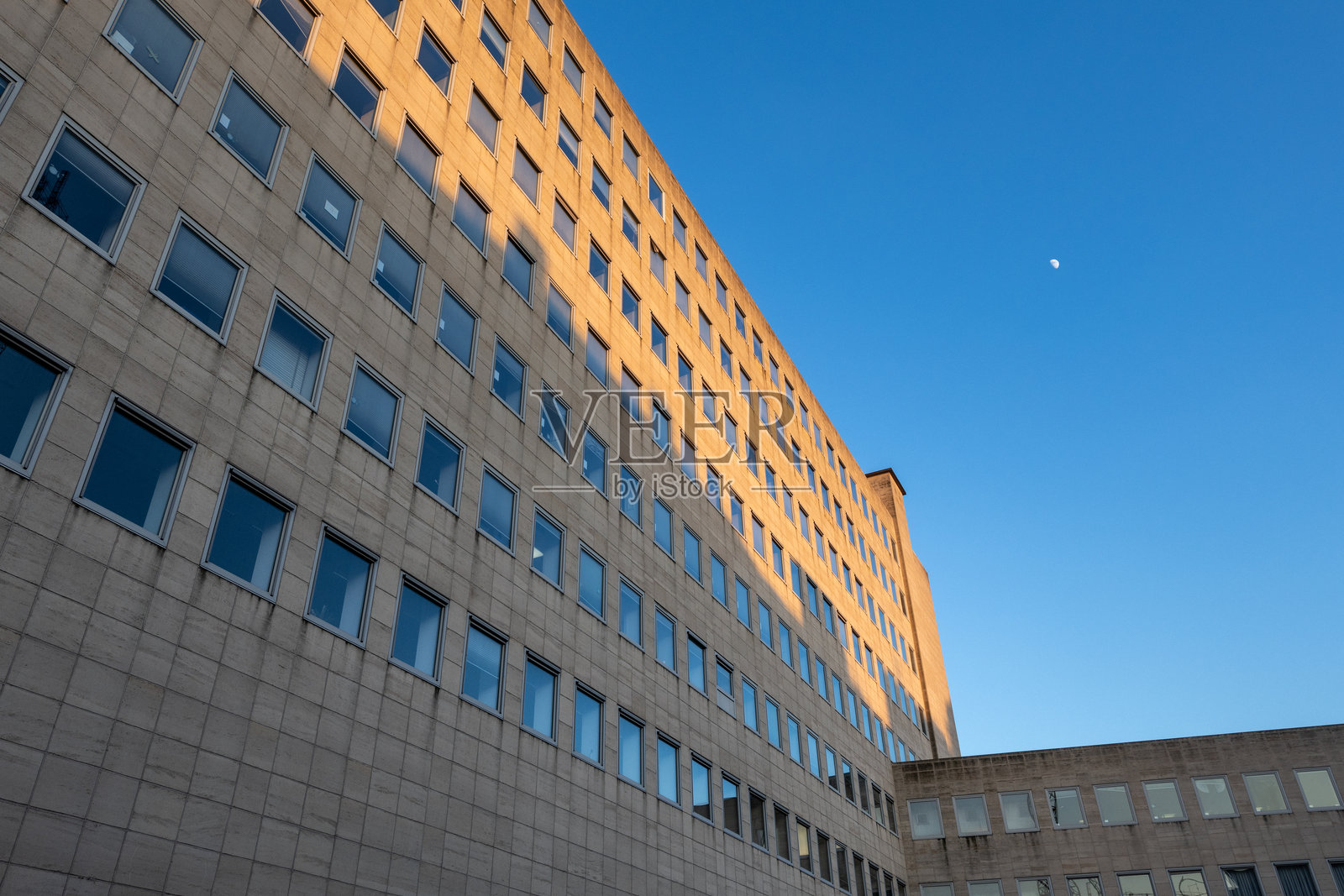 低角度拍摄的大楼，外部窗户在蓝天阳光下熠熠生辉。照片摄影图片