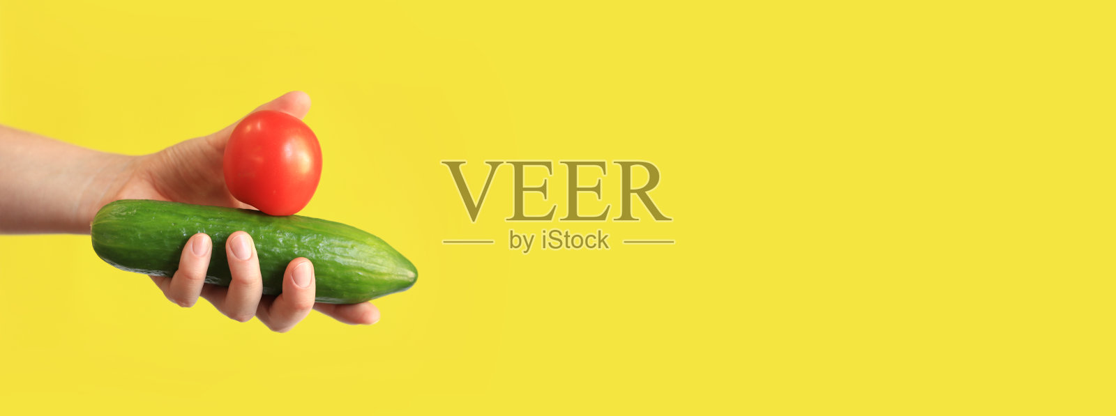 女性手中拿着黄背景上的黄瓜和红番茄照片摄影图片