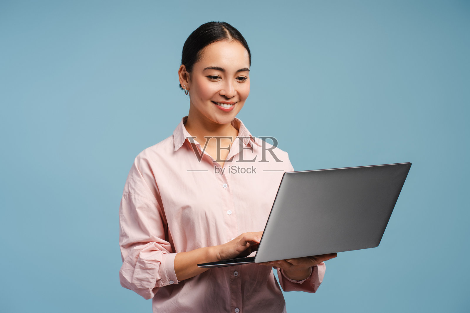 迷人微笑的亚洲职业女性在蓝色背景下微笑并在笔记本电脑上打字照片摄影图片