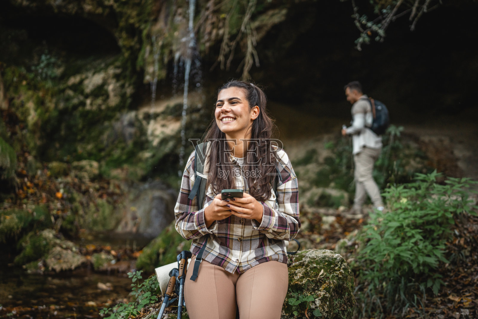 美丽的女性徒步旅行者在瀑布附近使用手机照片摄影图片