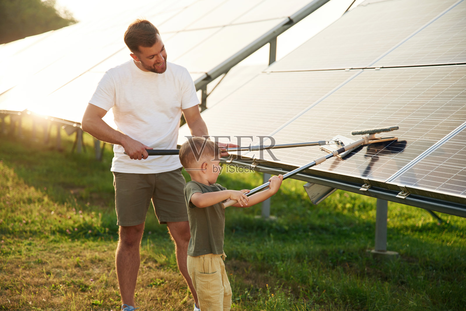 清洁表面的时刻。父亲和他的小儿子在太阳能电池板旁一起。照片摄影图片