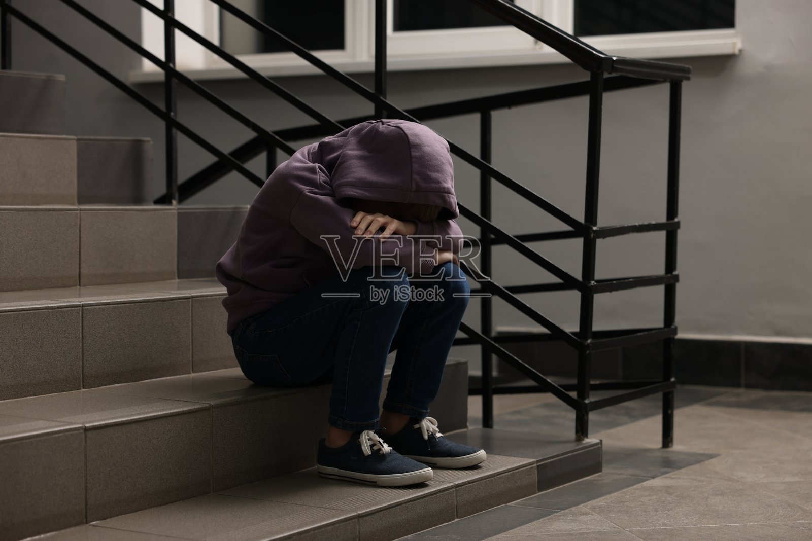 坐在室内楼梯上的沮丧男孩照片摄影图片