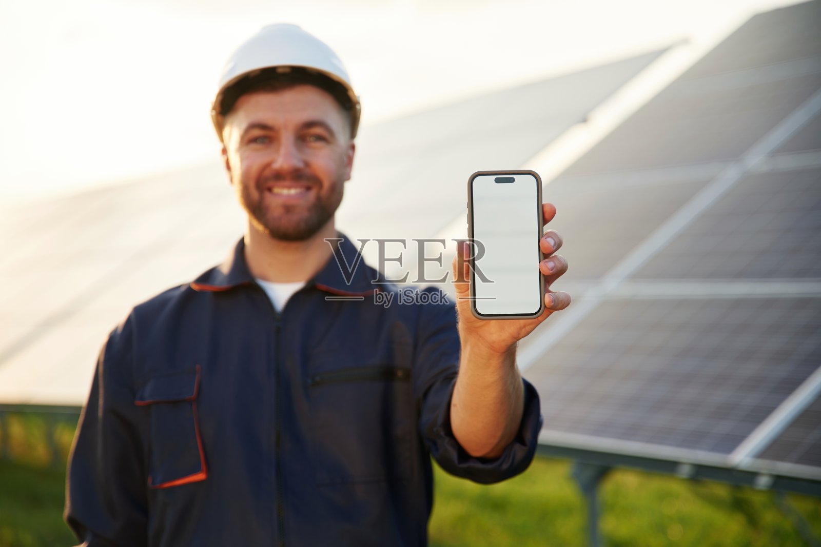 带有空白空间的智能手机。男子在户外白天与太阳能电池板一起工作。照片摄影图片