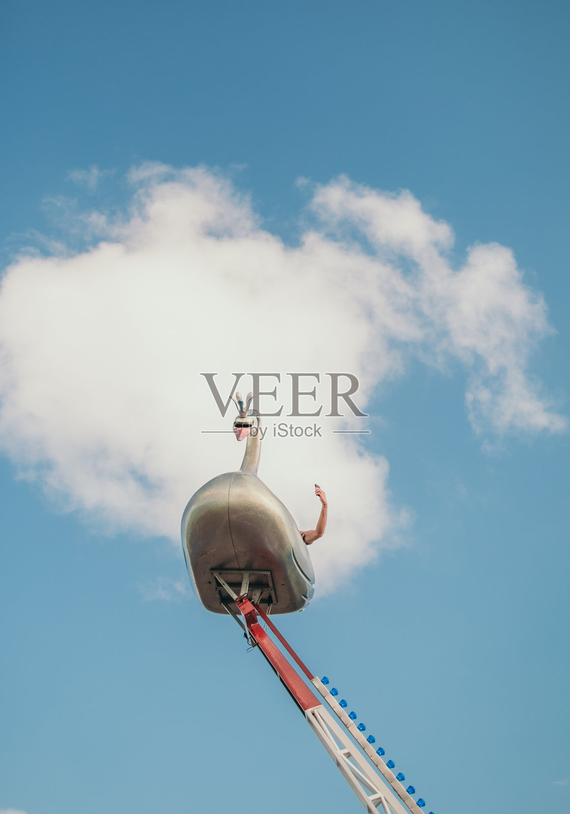 一座金属天鹅形状的游乐设施在蓝天和白云下。照片摄影图片