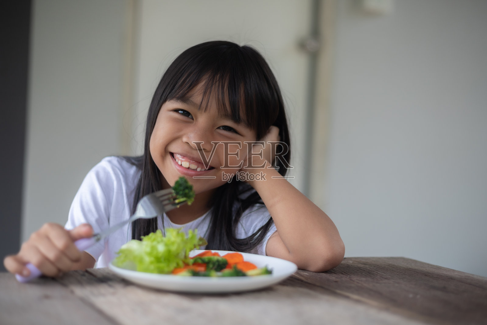 一个小女孩正在吃一盘蔬菜，包括西兰花和胡萝卜。照片摄影图片