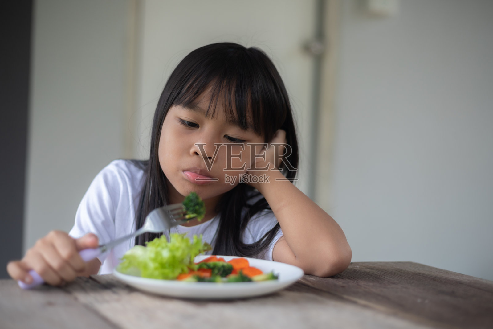 一个小女孩正在用叉子吃沙拉。照片摄影图片
