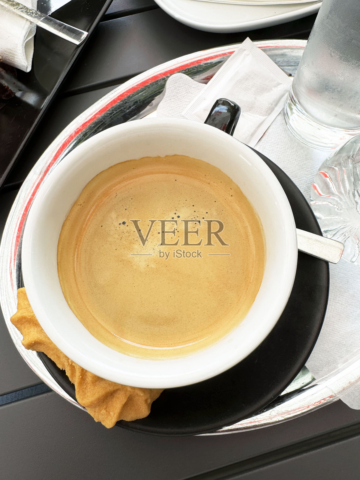 新鲜的浓缩咖啡配饼干和一杯水，放在时尚的托盘上，置于户外。照片摄影图片