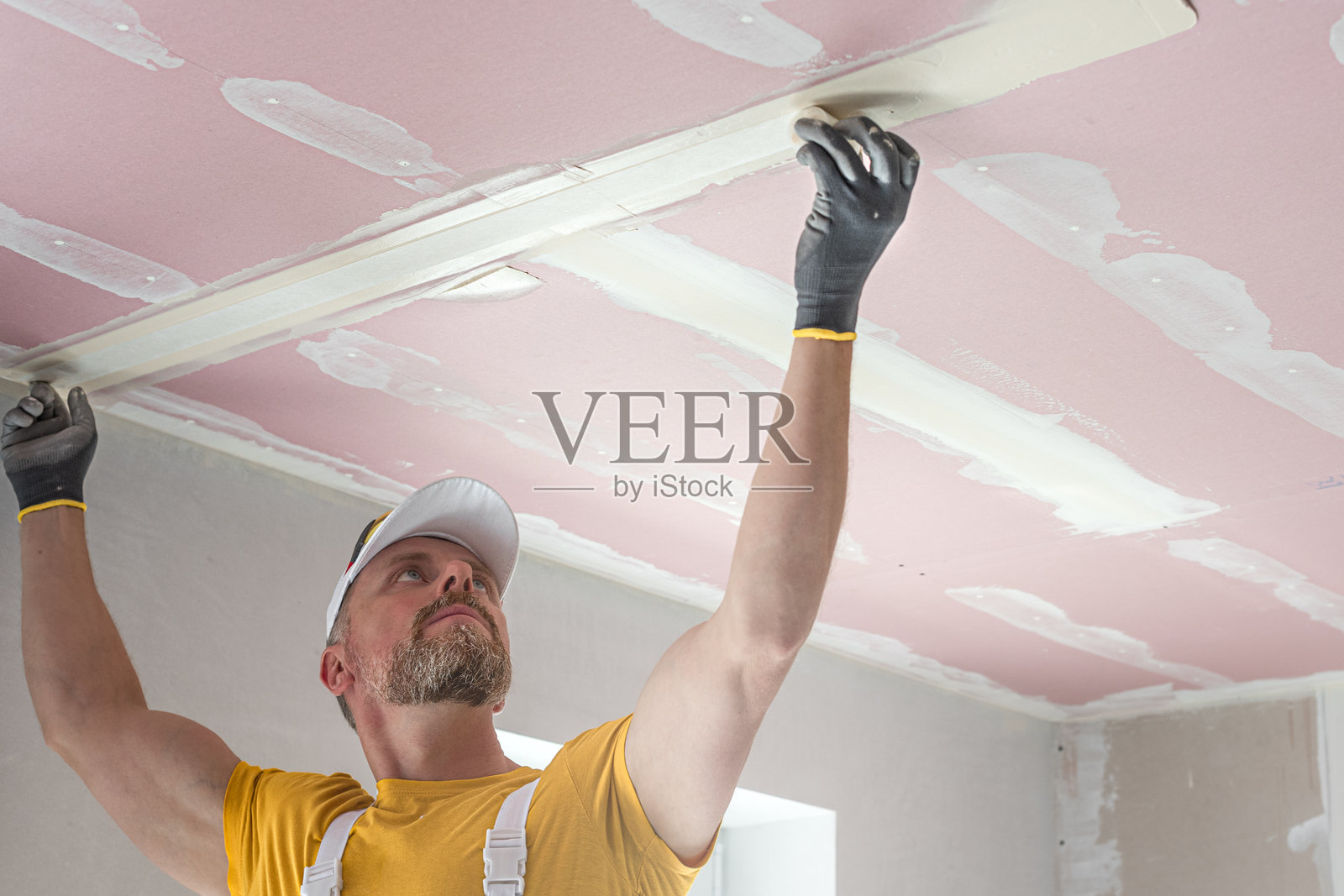 工人正在制作石膏板天花板。他正在对石膏板天花板的接缝进行贴带处理。他将玻璃纤维带插入腻子中。照片摄影图片