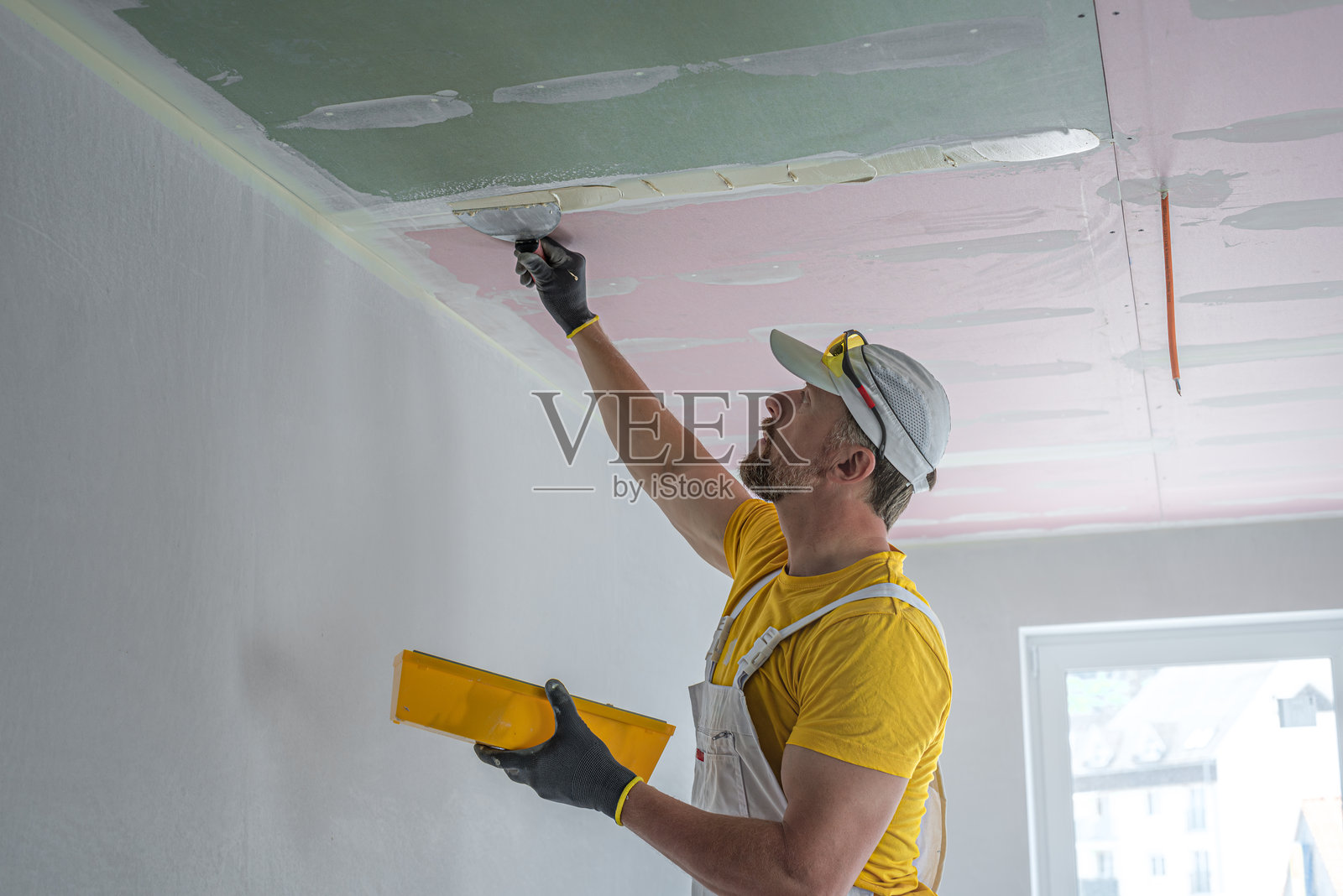 工人正在制作石膏板天花板。他在进行石膏板天花板接缝的贴带工作。他正在用石膏填料涂抹接缝。照片摄影图片