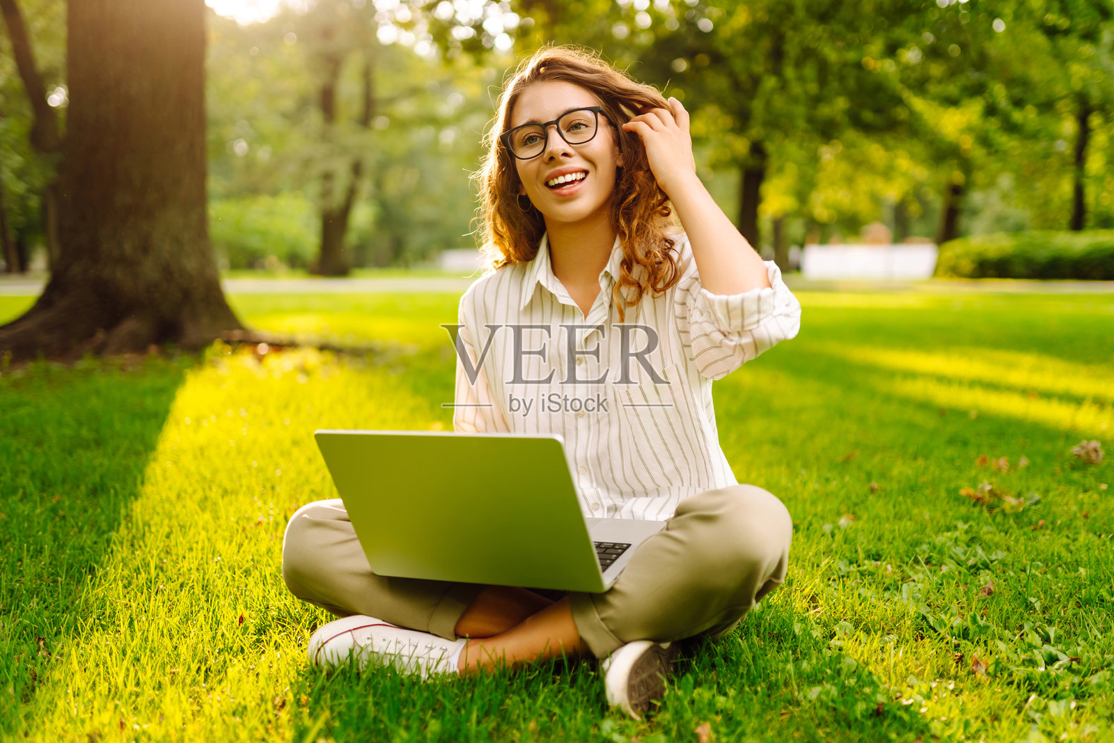 年轻女性坐在城市公园的绿草地上，使用笔记本电脑工作。照片摄影图片