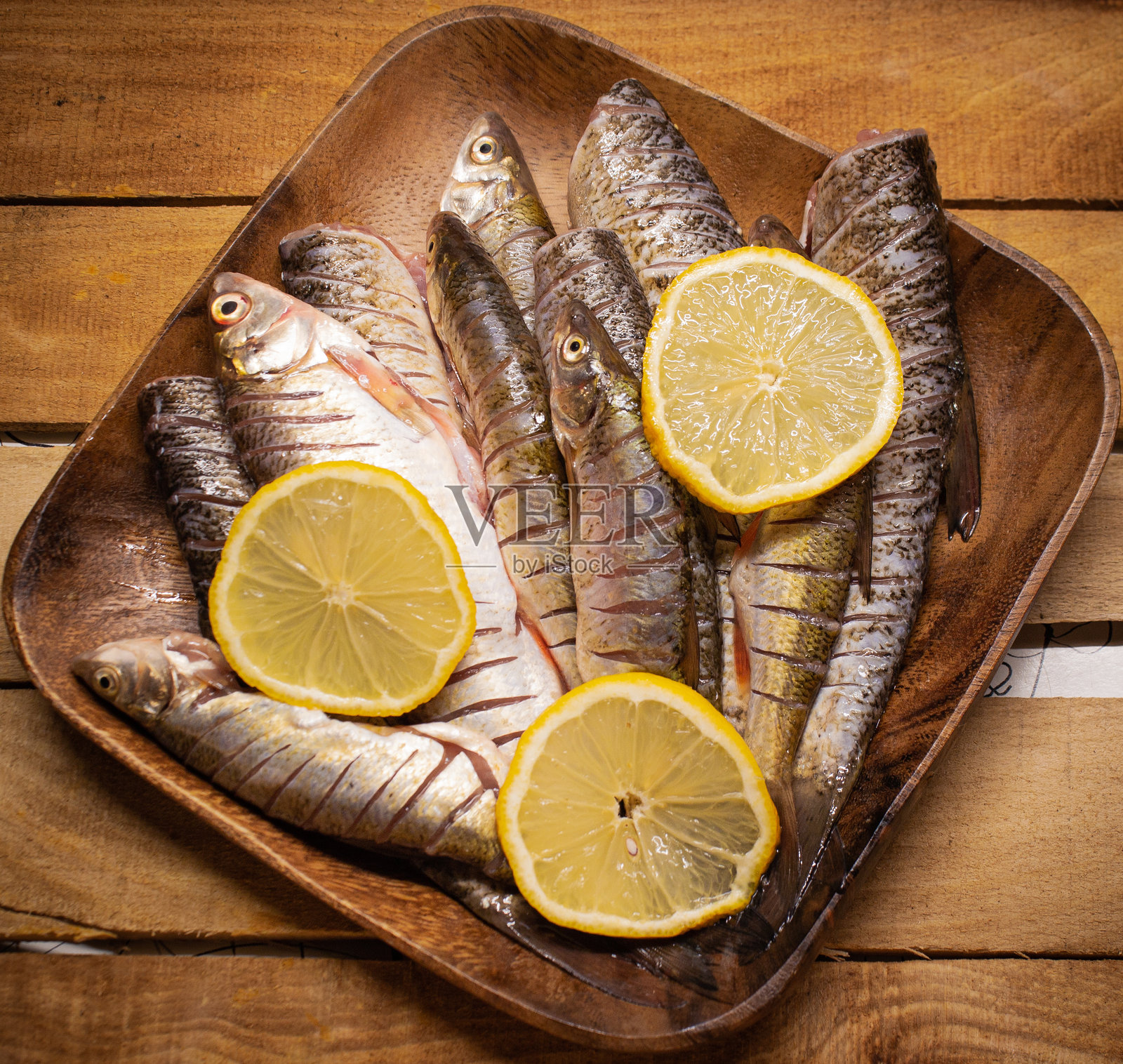 平铺的新鲜鲶鱼放在木质方盘上，背景是装饰有柠檬片的木质桌面。照片摄影图片