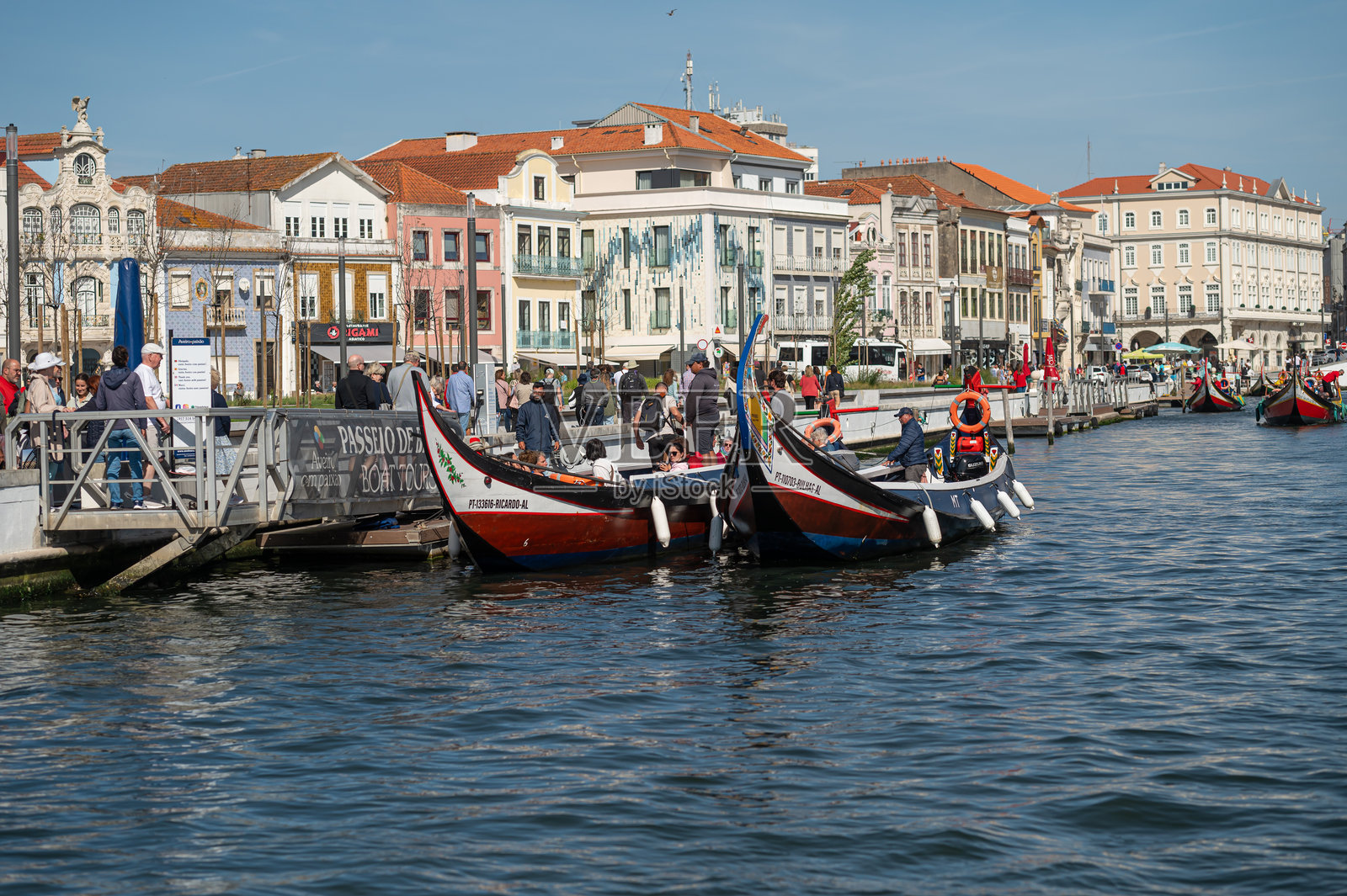 人们在葡萄牙阿威罗的运河旁享受阳光明媚的日子,乘坐传统小船。照片摄影图片