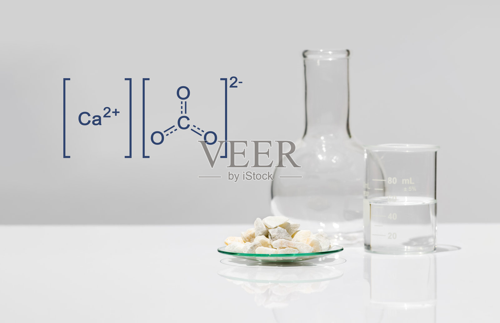 白色实验室桌上，化学观察皿中放置着碳酸钙颗粒，旁边是烧杯和平底烧瓶，分子结构图案位于一旁。侧视图。照片摄影图片