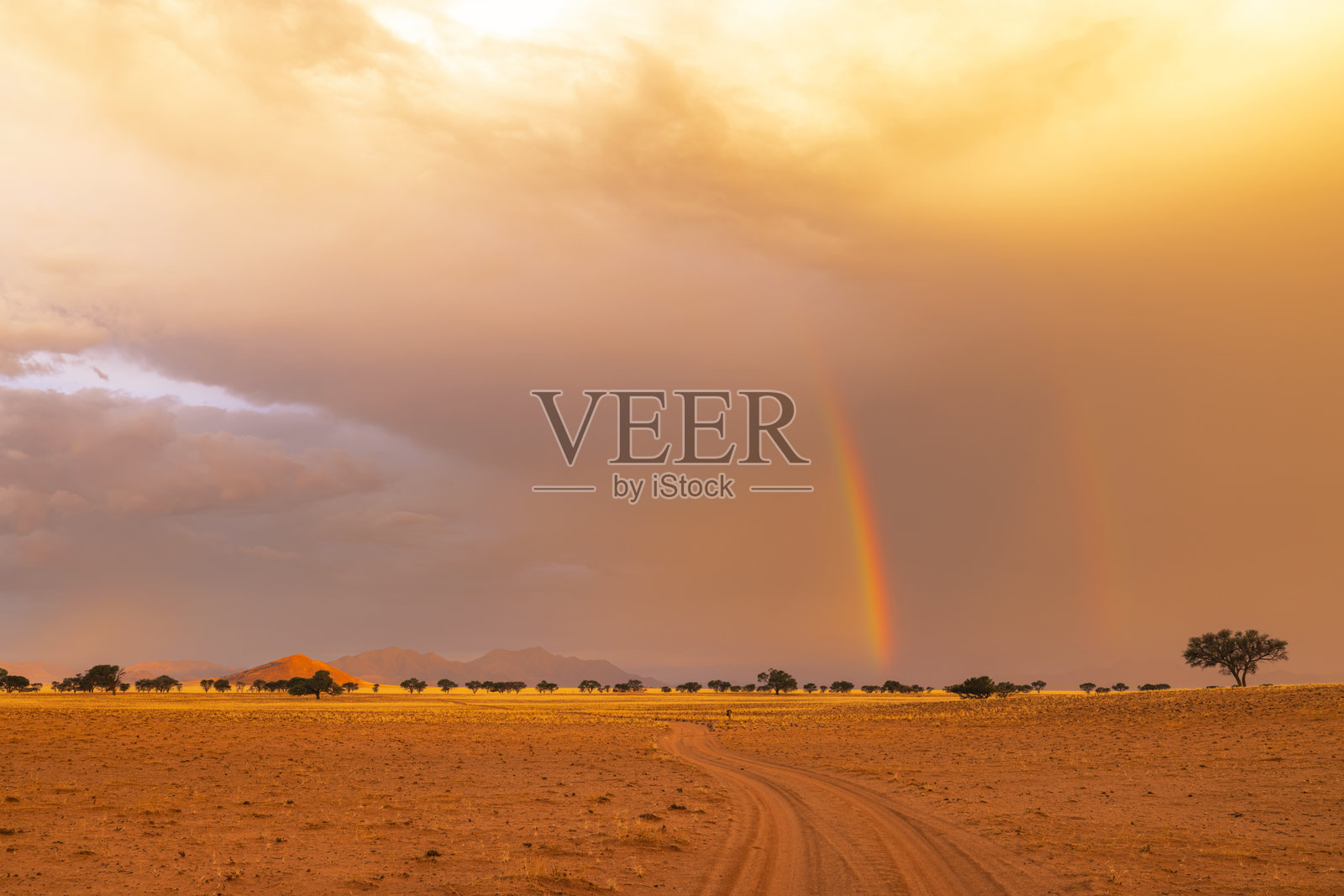 干燥沙漠沙土上方的彩虹和云朵照片摄影图片