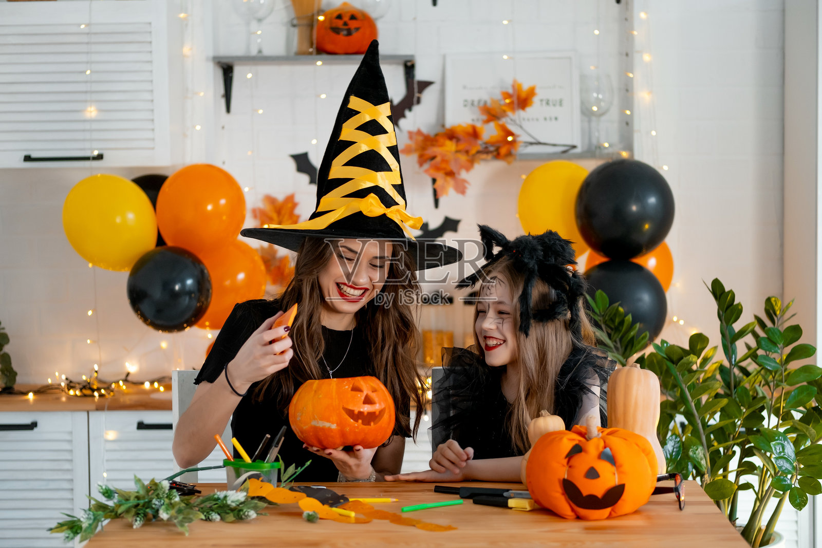 一个快乐的家庭正在为万圣节做准备。母亲和女儿在厨房里穿着节日服装，开心地一起绘画和雕刻南瓜，庆祝这个节日。照片摄影图片