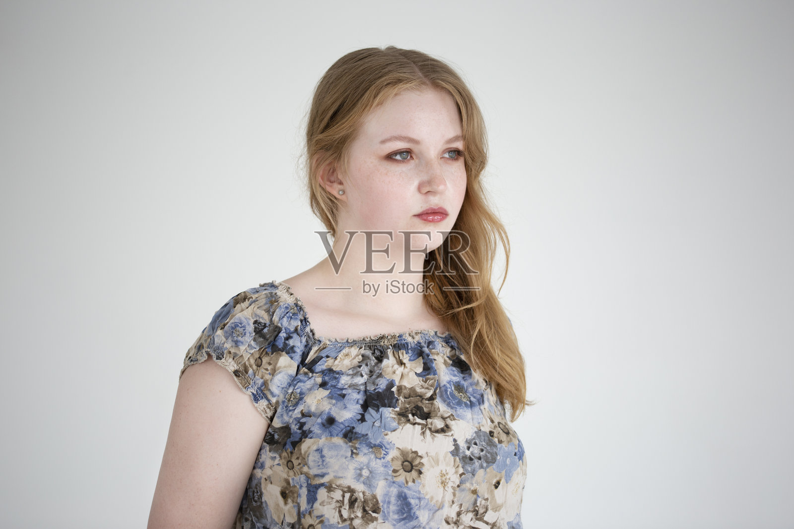 长发年轻女性在简单背景前，穿着花卉衬衫，深思熟虑地摆姿势。照片摄影图片