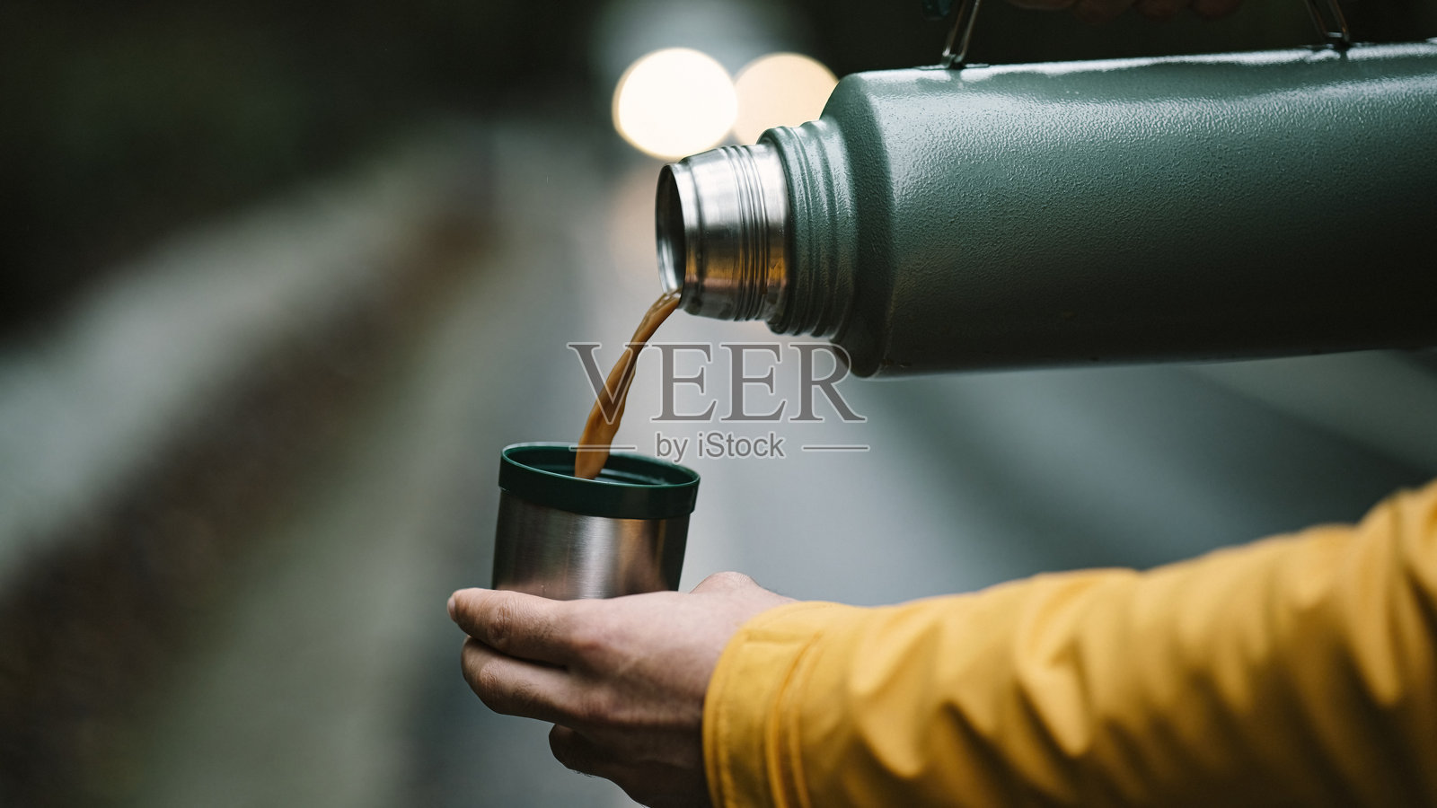 男人手部特写，从绿色保温瓶中倒咖啡到杯子里。金属不锈钢保温瓶在森林中的照片。照片摄影图片