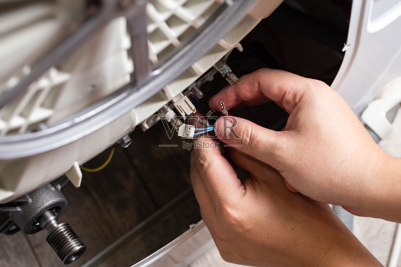 师傅的手拆卸电芯，以去除洗衣机的加热元件和加热传感器。洗衣机维修，工业。照片摄影图片