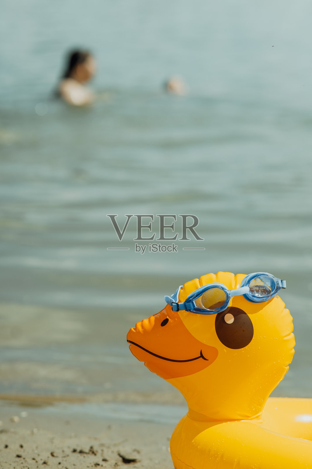 海滩上的黄色鸭子漂浮着，戴着游泳护目镜照片摄影图片