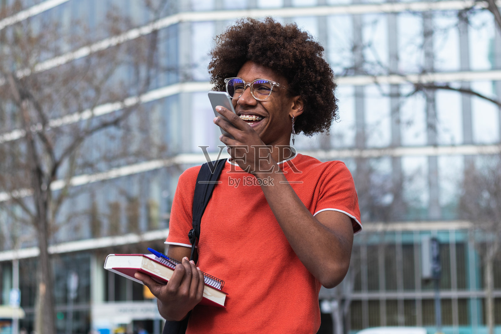 快乐的年轻黑人男孩在街上学习后用智能手机发送语音信息照片摄影图片