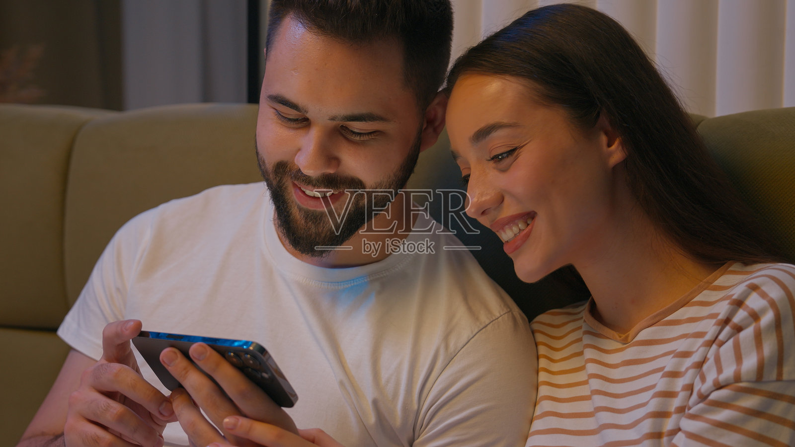 白人情侣男士女士男朋友女朋友一起在床上卧室里用手机智能手机设备欢笑微笑观看搞笑视频享受幽默浏览甜心配偶照片摄影图片