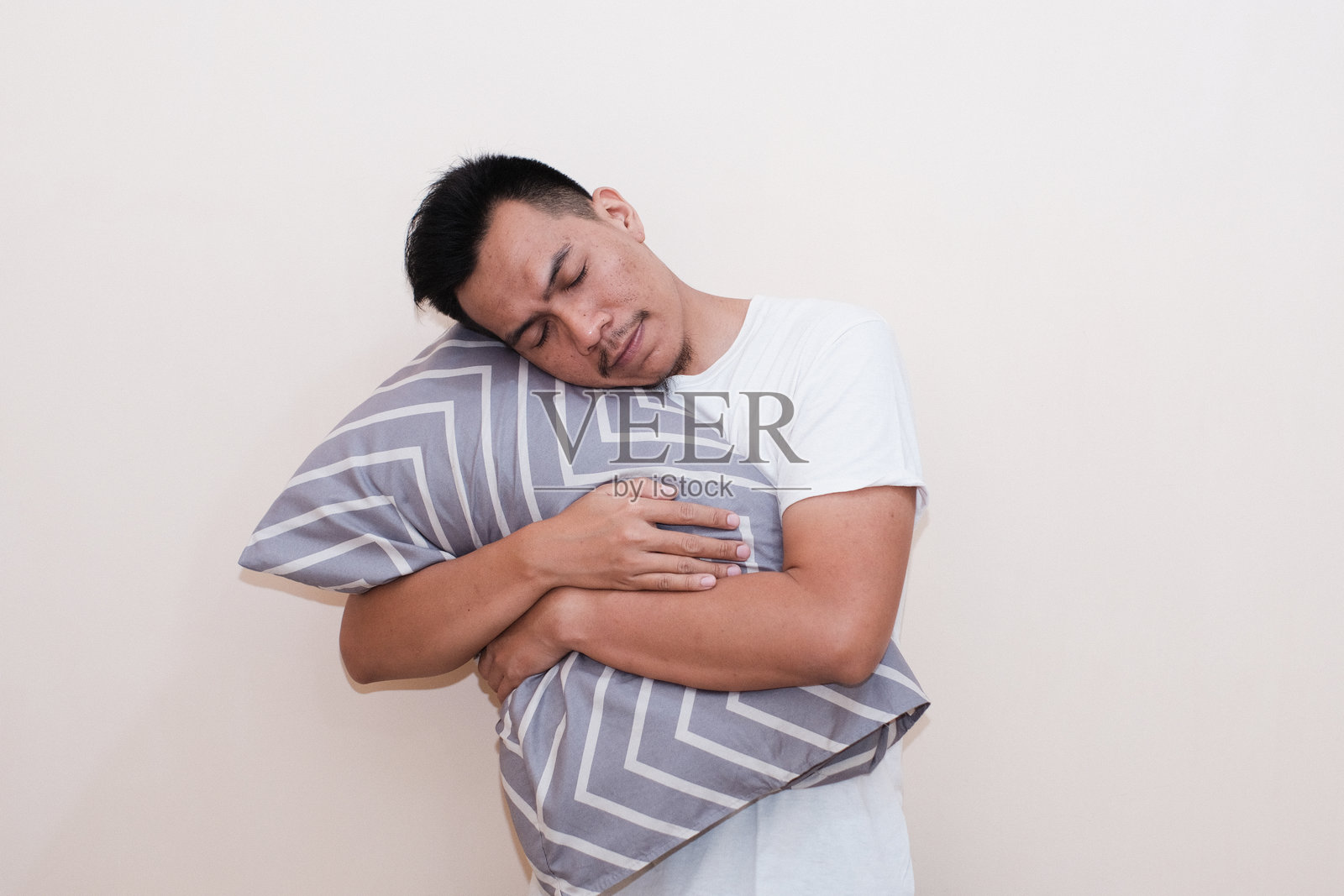 一位东南亚男子开心地微笑，抱着枕头，享受温馨的夜晚。照片摄影图片