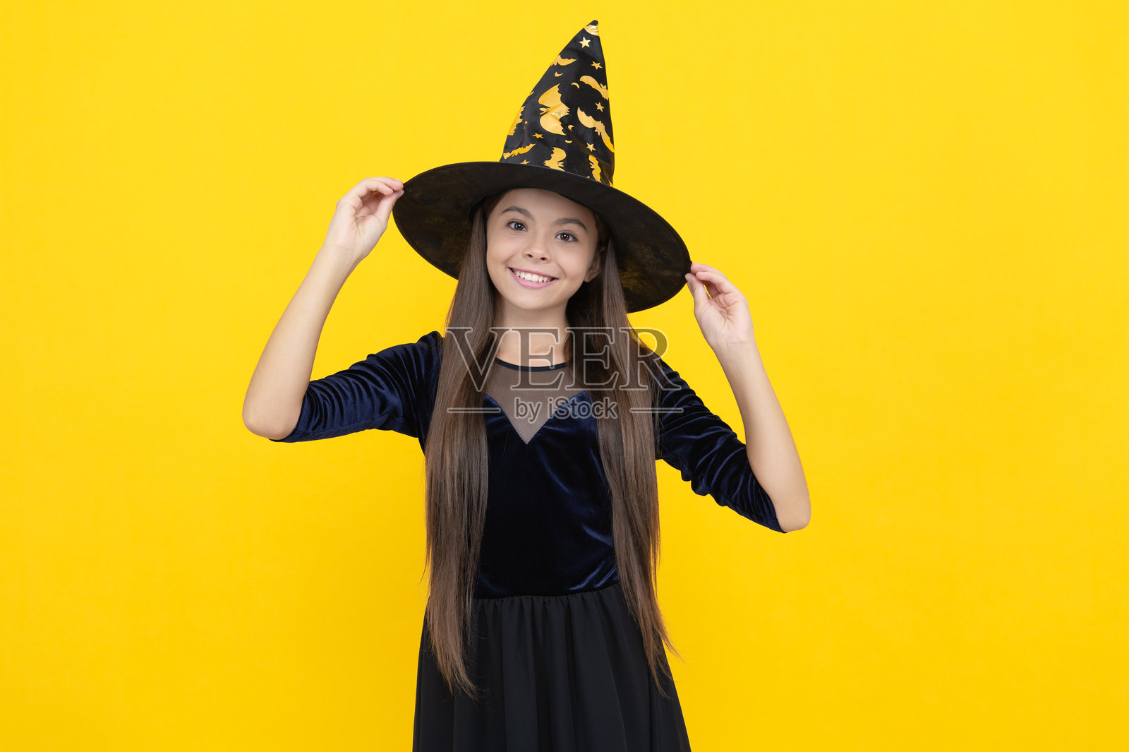 穿着女巫服装的少女。快乐的万圣节。女巫在黄色背景下的万圣节服装。讨糖或捣蛋。庆祝万圣节派对假日。万圣节。10月31日。恐怖的糖果。照片摄影图片