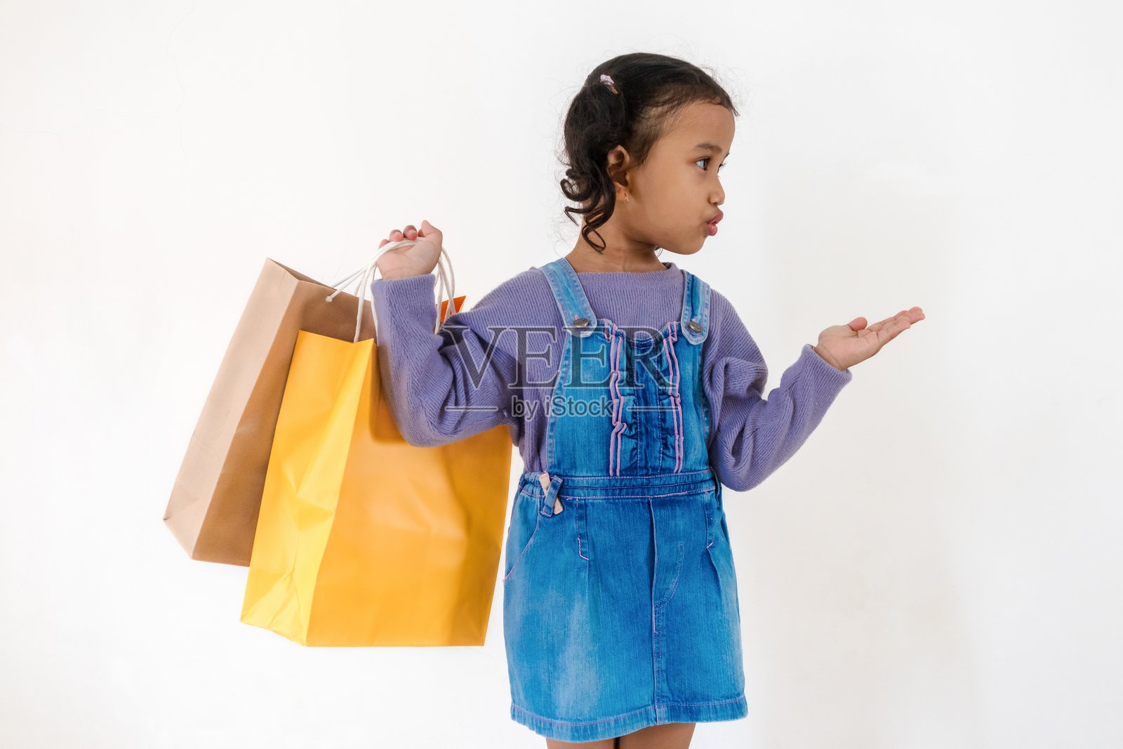 兴奋的小女孩用手指指着旁边，同时手里拿着一个纸购物袋。照片摄影图片