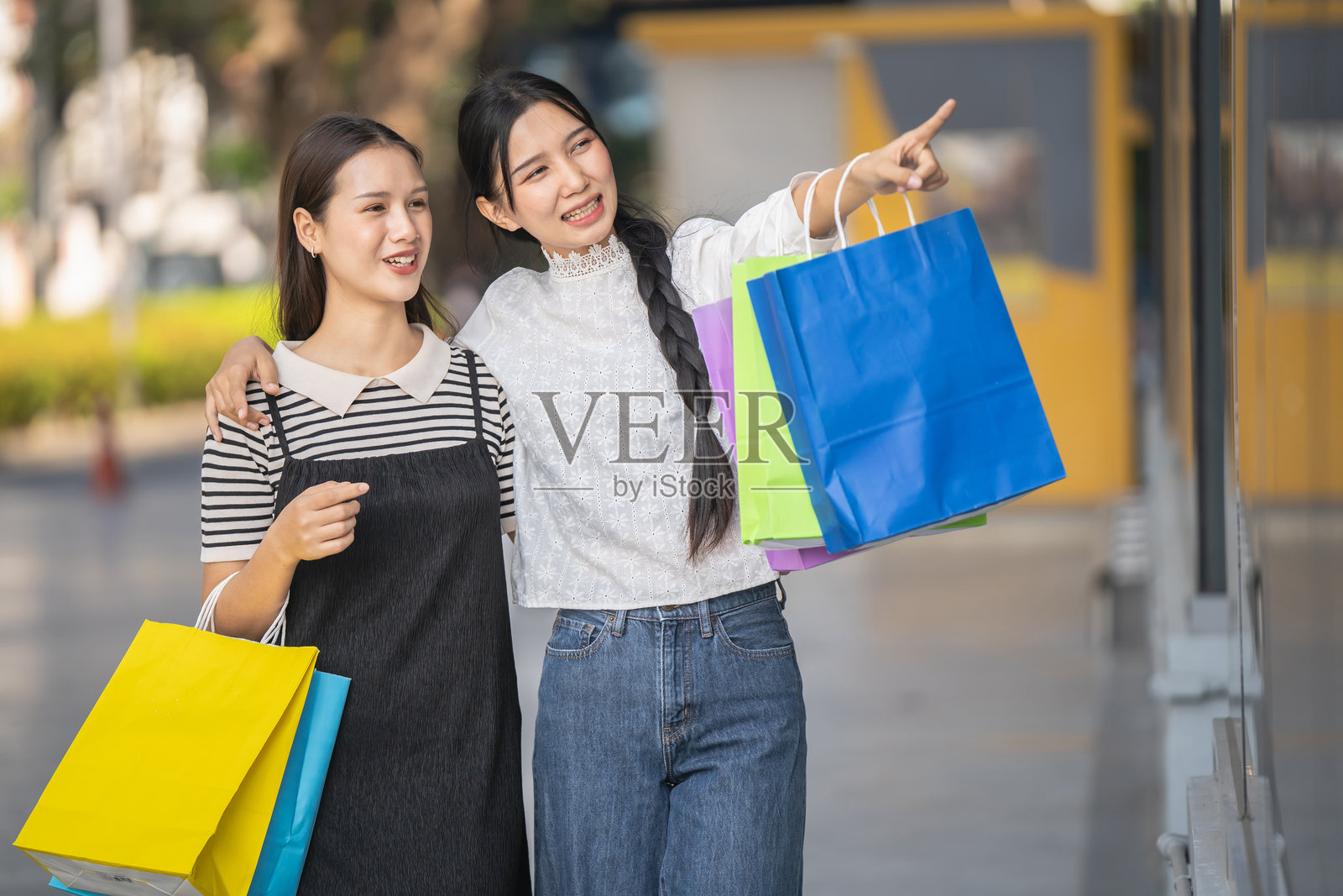 两个快乐的亚洲女性穿着时尚服装，手提购物袋，在购物中心前走。照片摄影图片